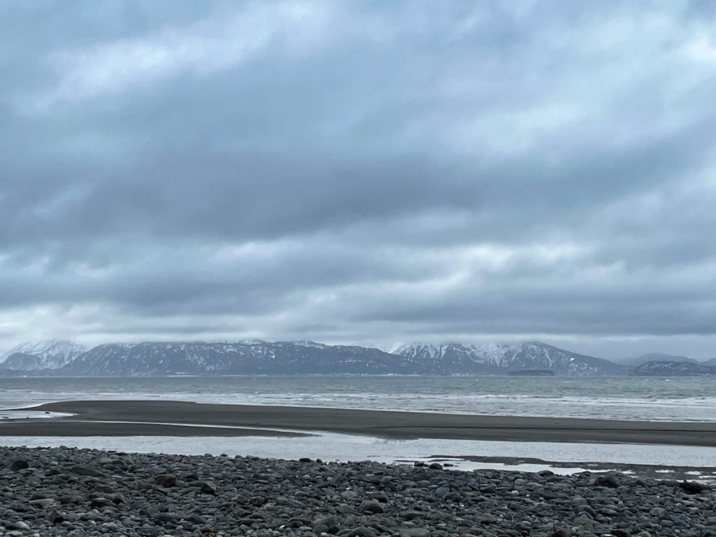 Grey beach with cobbles in foregrowns and lowered clouds over mountains